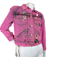 Angled front view of Marc Jacobs Paradise bright pink cropped denim jacket with black acid wash finish, embroidered patches and decorative pins.