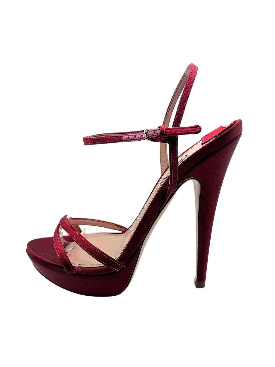 Side detail of Miu Miu burgundy satin platform heel showing the adjustable metal buckle, slim ankle straps and satin-covered stiletto.