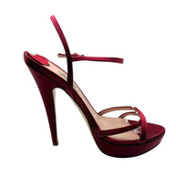 Outer side profile of a Miu Miu burgundy satin platform sandal featuring a slender stiletto heel, crisscross toe straps and raised sole.