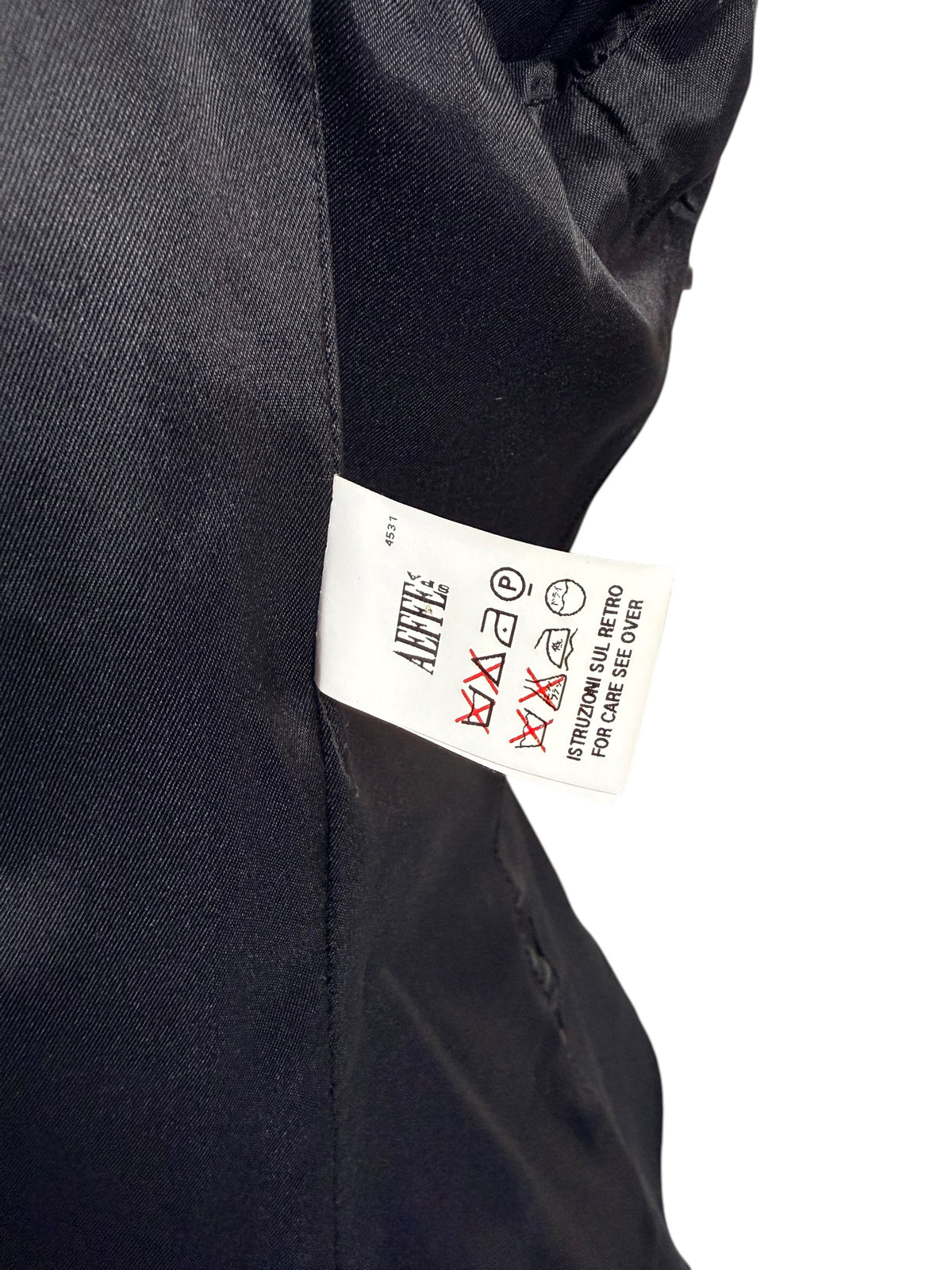 Interior care label of Moschino black tailored peplum jacket showing international garment care symbols, professional cleaning instructions and black lining.