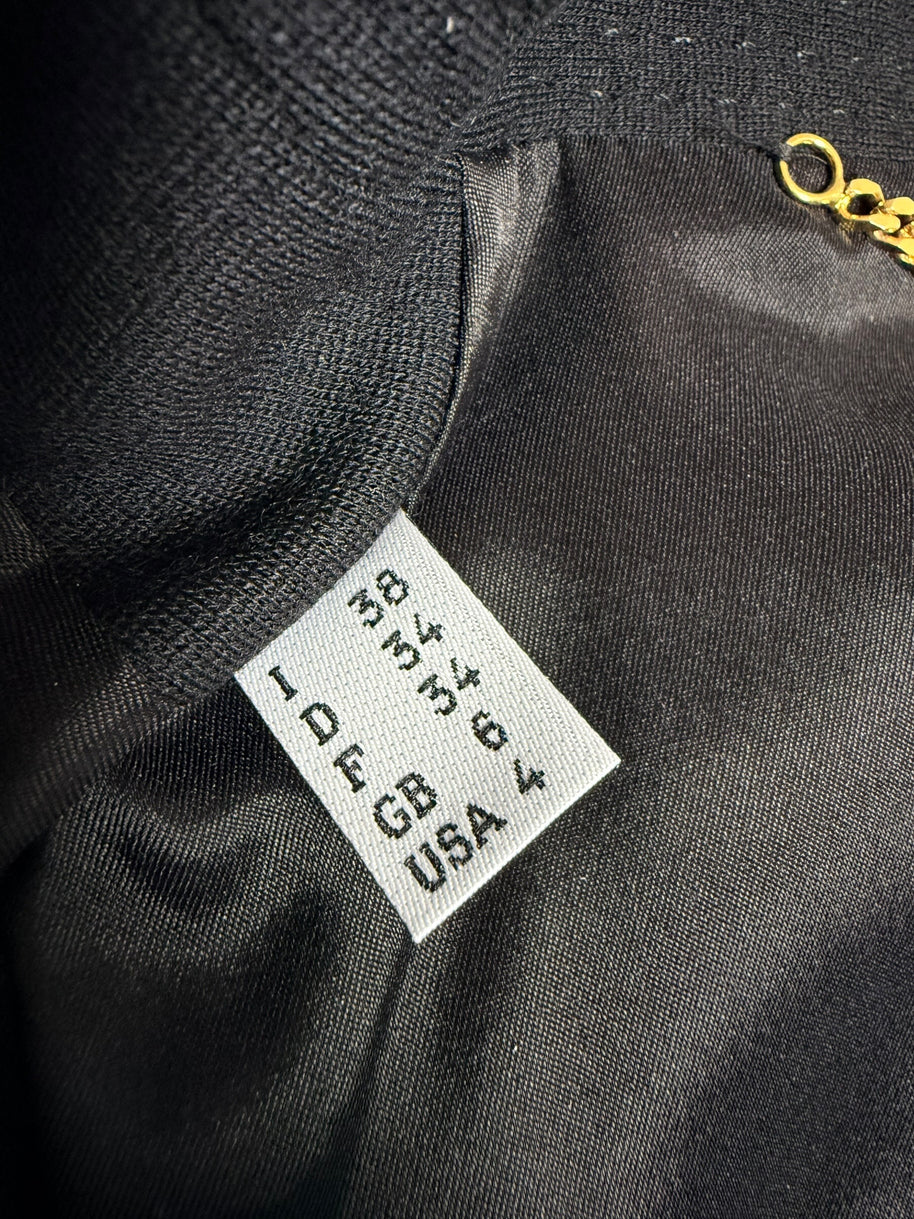 Close-up of Moschino black peplum jacket size label showing Italian 38, French 34, German 34, UK 6 and USA 4 sizing against the black lining.