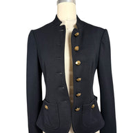 Moschino black tailored peplum jacket shown unbuttoned on a dress form, featuring a stand collar, faceted gold-tone buttons and rounded front pockets.