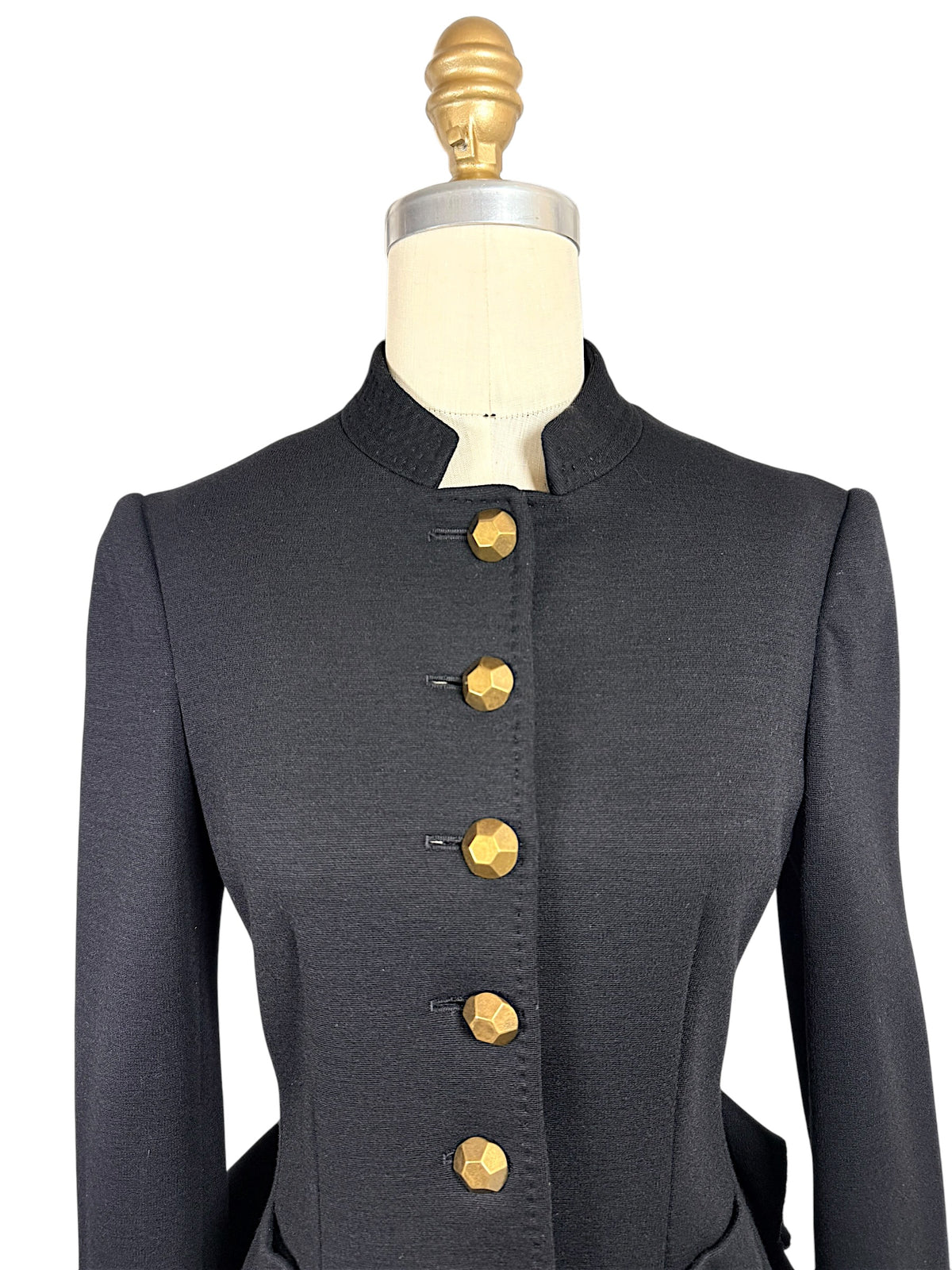 Close-up of Moschino black tailored jacket showing the high stand collar, structured shoulders, fitted front seams and faceted gold-tone buttons.