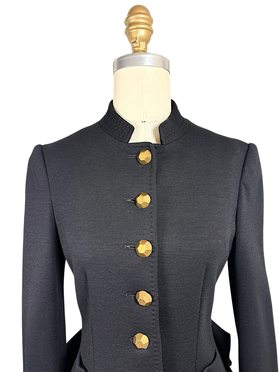 Close-up of Moschino black tailored jacket showing the high stand collar, structured shoulders, fitted front seams and faceted gold-tone buttons.