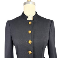 Close-up of Moschino black tailored jacket showing the high stand collar, structured shoulders, fitted front seams and faceted gold-tone buttons.
