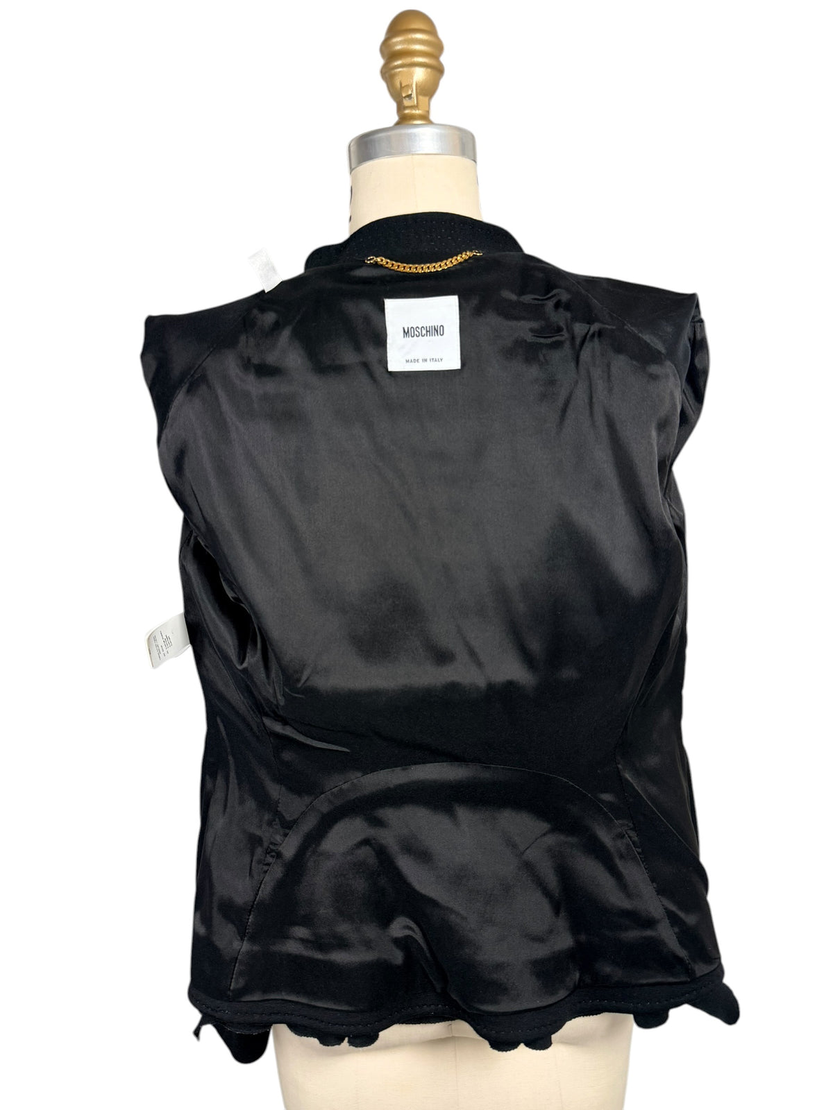 Interior view of Moschino black peplum jacket showing the smooth black lining, Moschino Made in Italy designer label, neckline chain and interior construction.