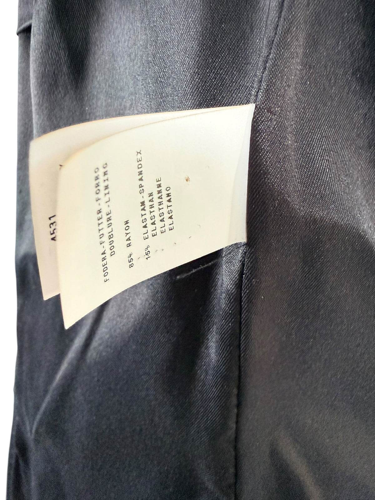 Close-up of Moschino black jacket composition label showing 85% rayon and 15% elastane-spandex, with the smooth black interior lining visible.