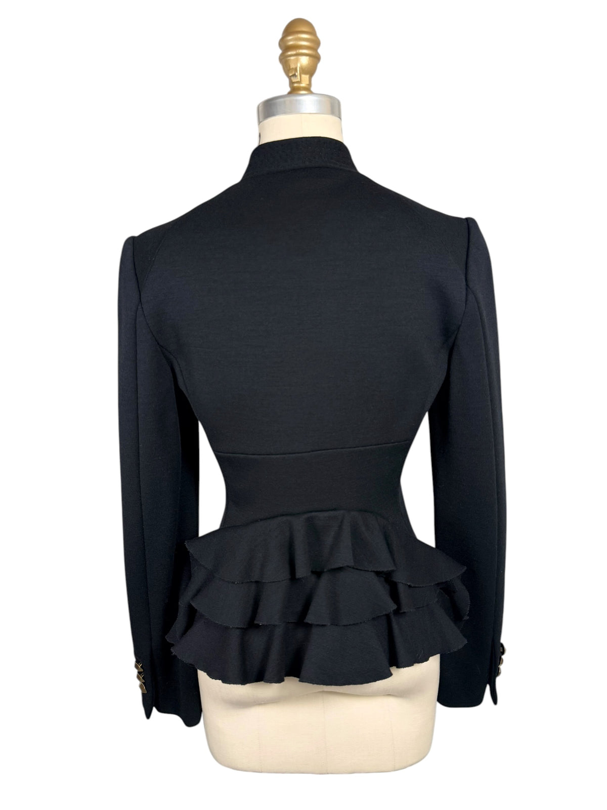 Full back view of Moschino black designer jacket featuring a sharply fitted waist and dramatic cascading tiers of fabric ruffles across the peplum hem.