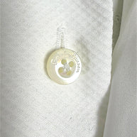 Macro detail of a lustrous Ralph Lauren engraved button on the white cotton tuxedo shirt, showing fabric texture and stitching.