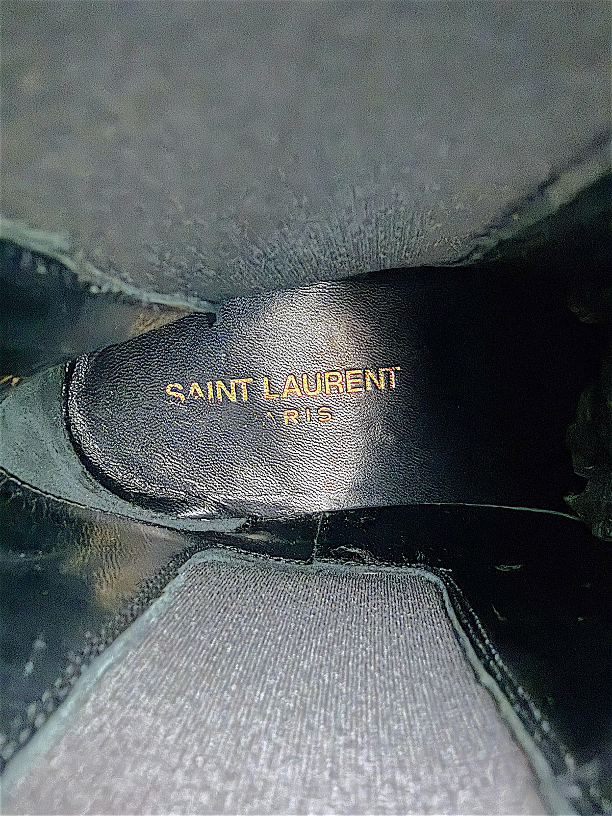 Interior of Saint Laurent Paris black leather Chelsea ankle boot showing gold Saint Laurent Paris designer logo stamped on the black leather insole.