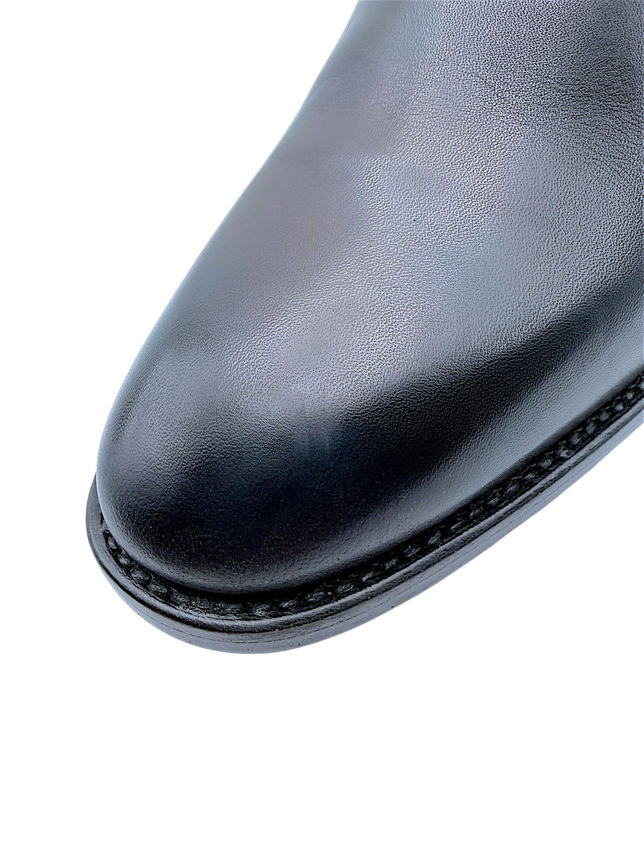 Close-up of Saint Laurent Paris Chelsea boot showing smooth black leather with light scuff on almond toe, fine welt stitching and subtle surface texture.