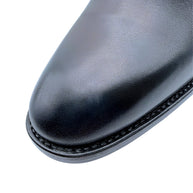 Close-up of Saint Laurent Paris Chelsea boot showing smooth black leather with light scuff on almond toe, fine welt stitching and subtle surface texture.