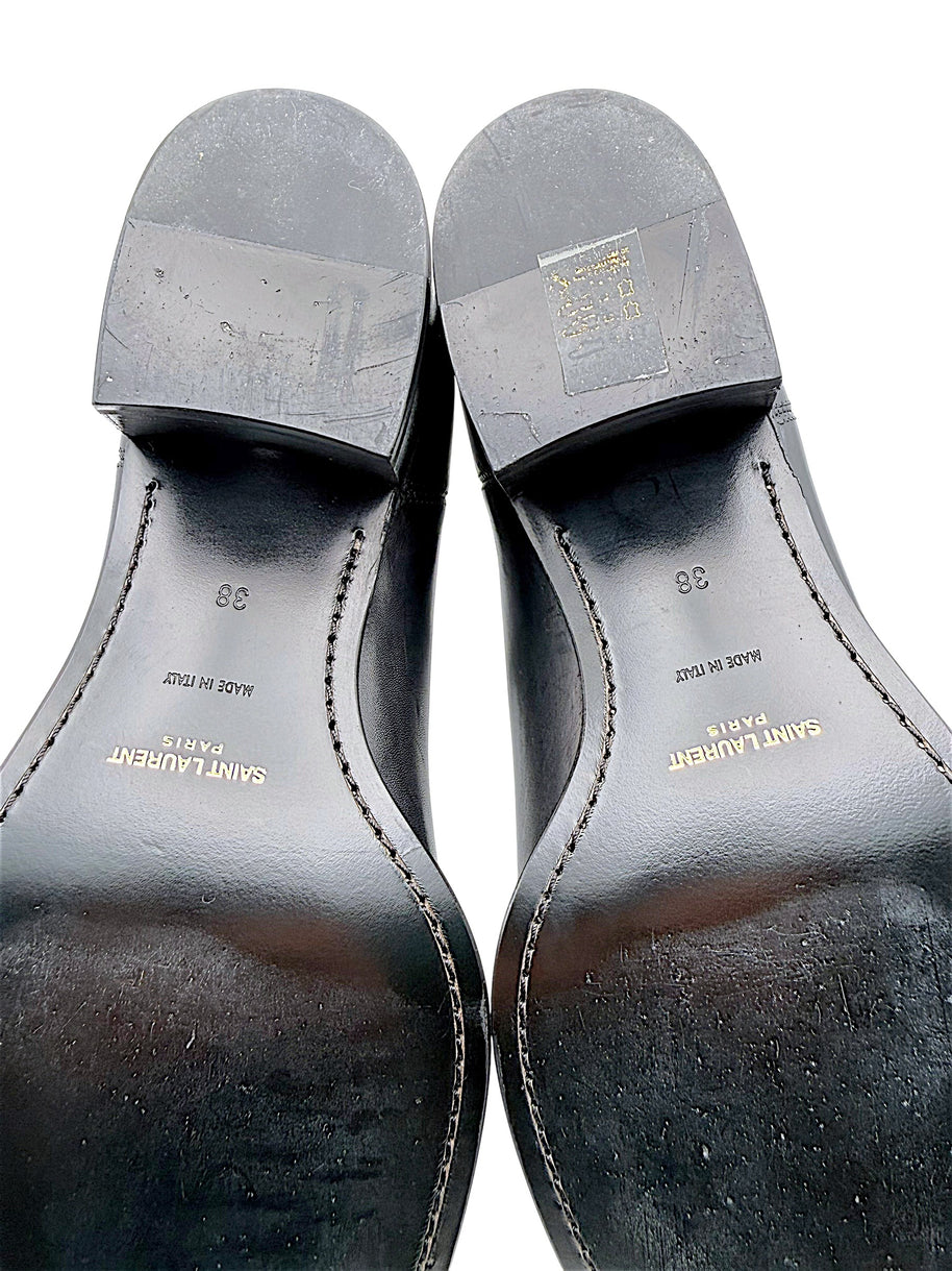 Detailed view of Saint Laurent Paris black leather Chelsea boot soles showing gold designer logos, Made in Italy stamps, European size 38 and surface wear on stacked heels and leather outsoles.