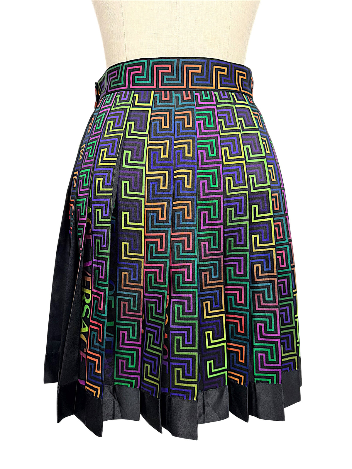 Back view of Versace Fall Winter 2021 La Greca pleated skirt showing multicolor geometric print, structured pleats and contrasting black hem.
