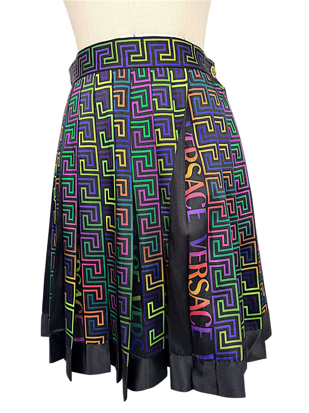 Versace FW 2021 high-waisted pleated skirt showing vibrant La Greca geometric print, multicolor VERSACE logo panels and black satin-effect hem.