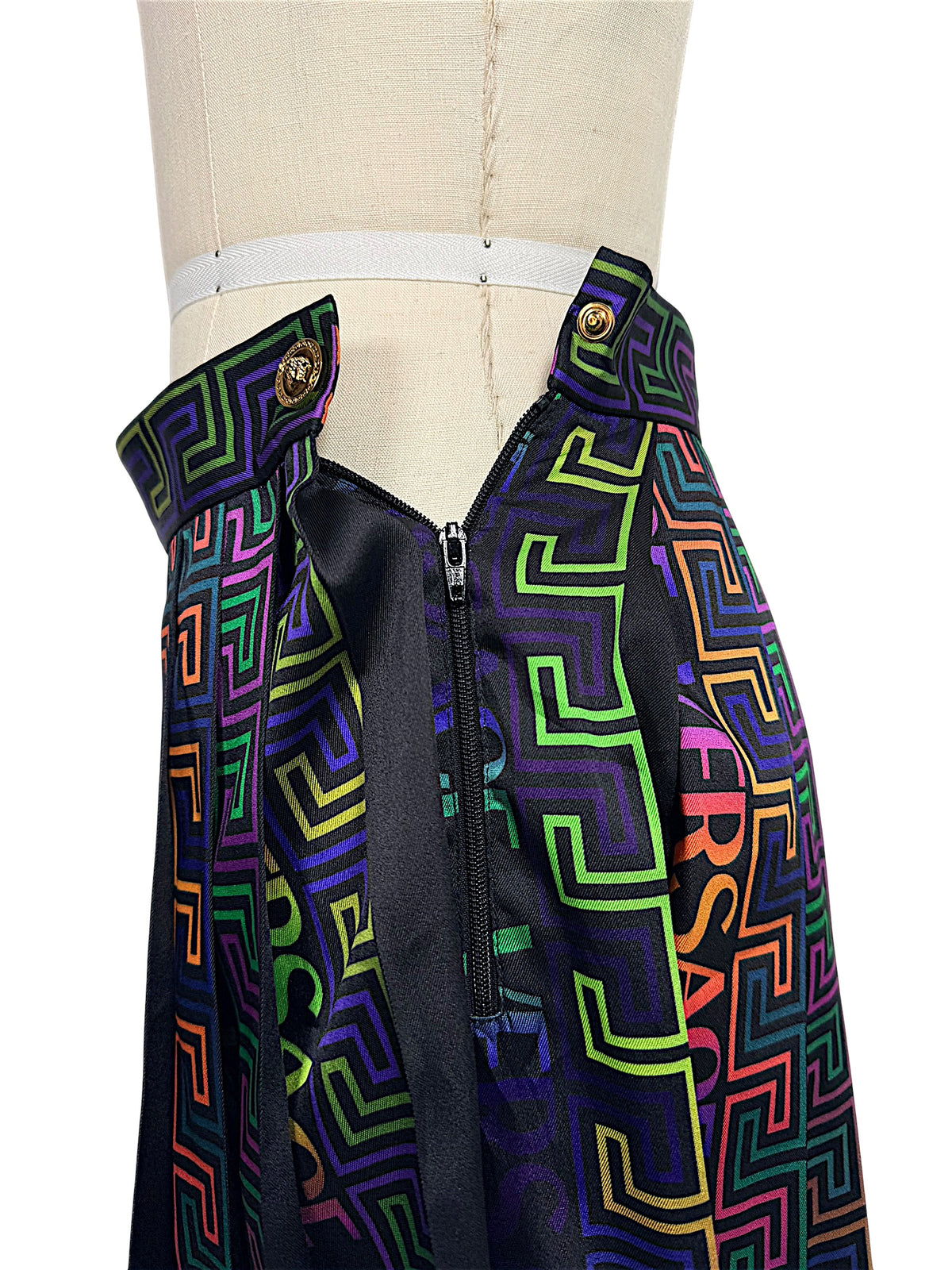 Close-up of Versace La Greca pleated skirt side zipper, Medusa button fastening and multicolor geometric print waistband.