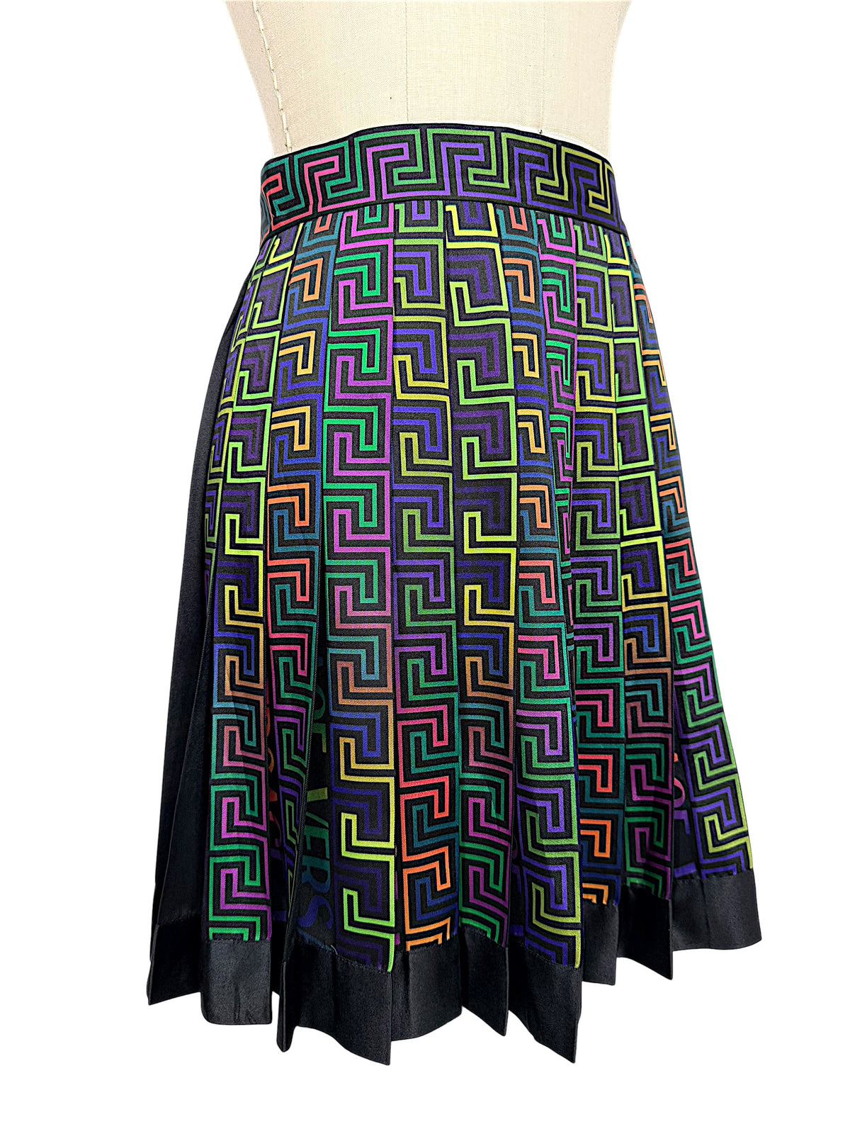 Angled front view of Versace Fall Winter 2021 La Greca skirt with structured A-line pleats, colorful geometric pattern and contrasting black hem.