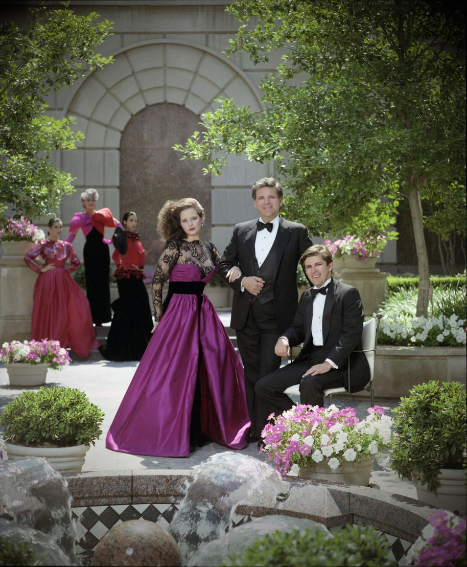 Archival photograph of American fashion designer Victor Costa with models wearing his signature eveningwear during the late 1980s, illustrating the glamorous era and design aesthetic associated with his formal collections. This image is provided for historical context and does not depict the featured gown.