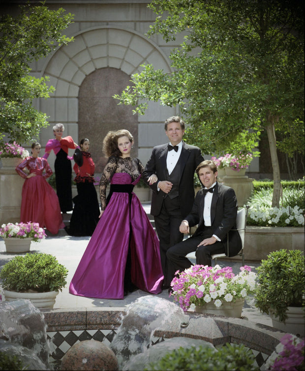 Archival photograph of American fashion designer Victor Costa with models wearing his signature eveningwear during the late 1980s, illustrating the glamorous era and design aesthetic associated with his formal collections. This image is provided for historical context and does not depict the featured gown.