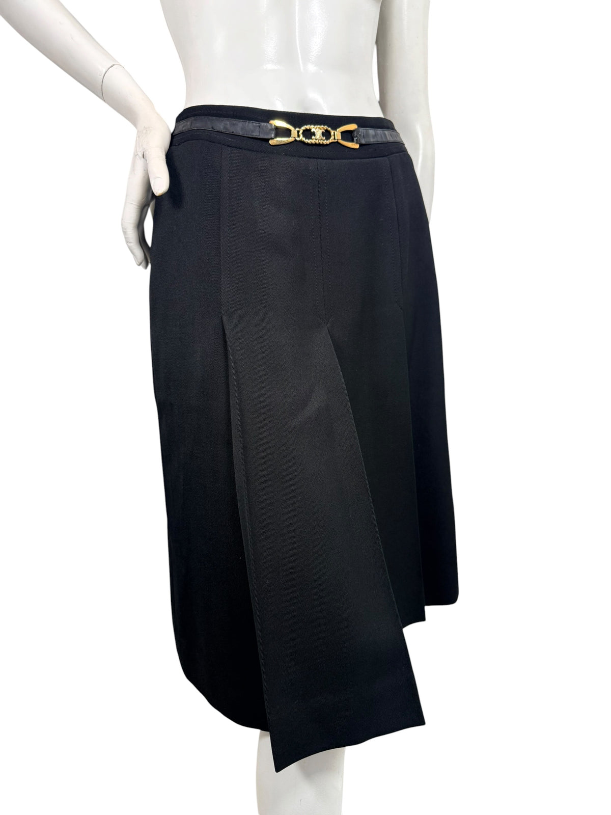 Angled front view of vintage Céline black wool midi skirt highlighting deep inverted pleats, overlapping panels, and gold-tone logo belt.