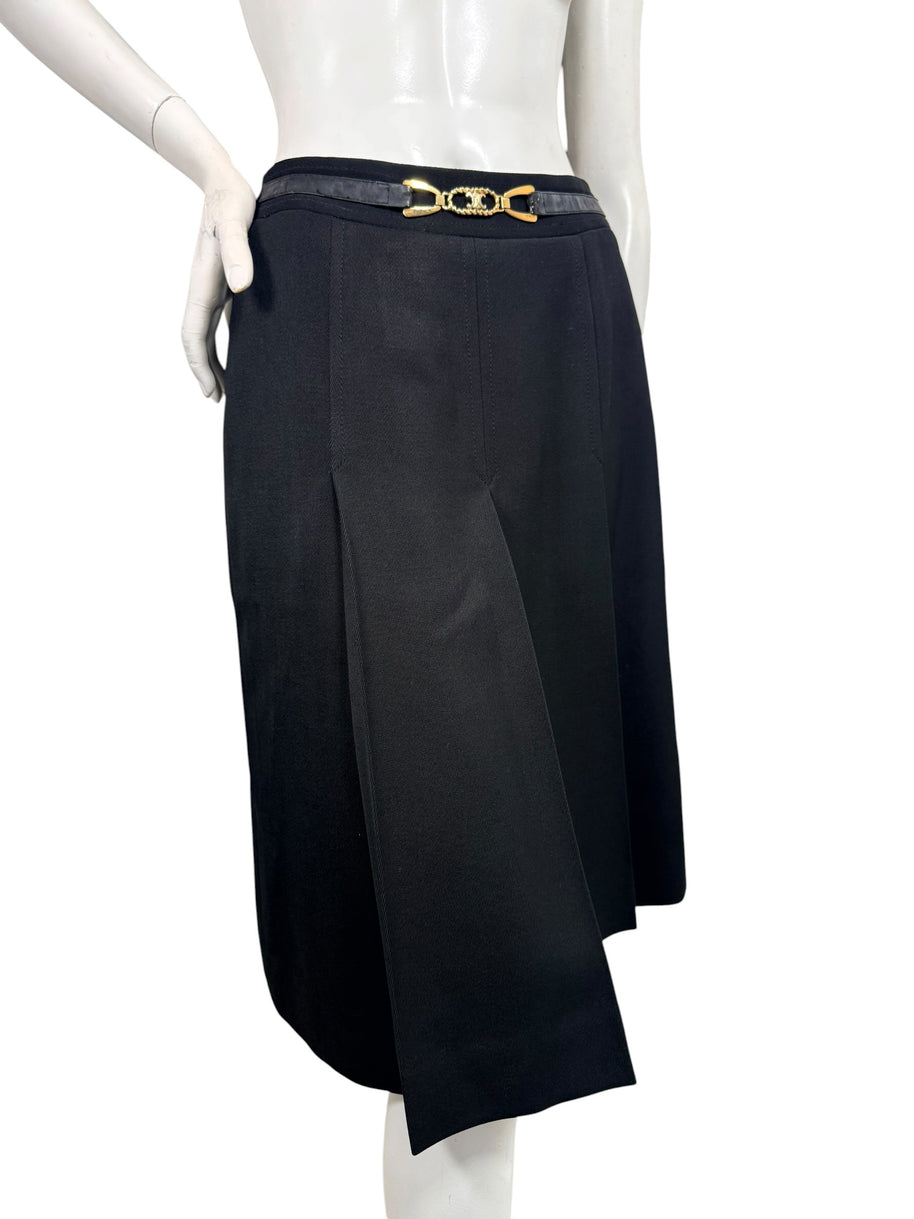 Angled front view of vintage Céline black wool midi skirt highlighting deep inverted pleats, overlapping panels, and gold-tone logo belt.