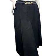 Angled front view of vintage Céline black wool midi skirt highlighting deep inverted pleats, overlapping panels, and gold-tone logo belt.