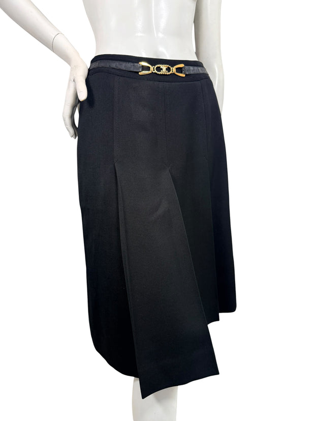 Angled front view of vintage Céline black wool midi skirt highlighting deep inverted pleats, overlapping panels, and gold-tone logo belt.