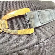 Macro detail of Céline engraving on gold-tone belt hardware showing light surface wear and creasing to the black leather waistband.