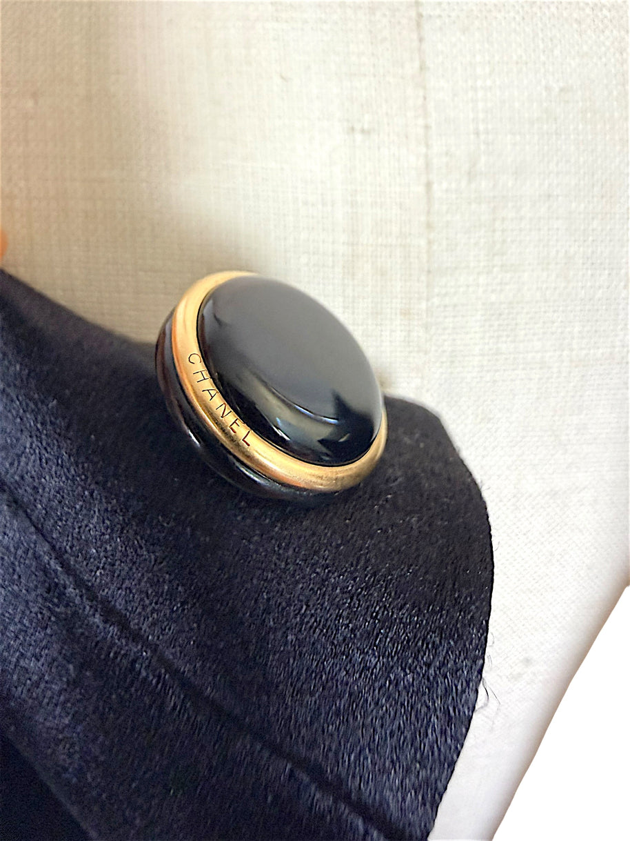 Macro detail of authentic vintage Chanel black enamel and gold-tone logo button.