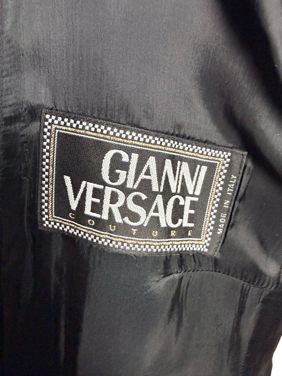 Close-up of the original Gianni Versace Couture woven designer label with black and white checkered border, gold detailing and Made in Italy marking inside a vintage black blazer.